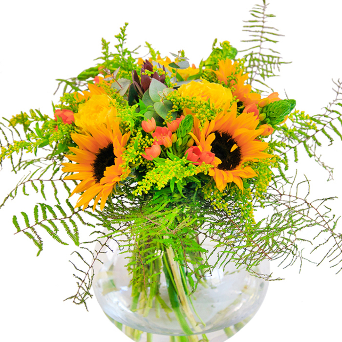 The impression radiating from this arrangement is pure jubilance, much like a walk through Barbican's lushly planted terraces on a sunny day. Towering at the centre, bold sunflowers spread out their sunny petals, each detailed with a velvety espresso-hued core, exuding a sense of optimism and unrestrained brightness. Luxurious yellow garden roses blossom alongside, their harmonious spirals echoing the architectural lines of Barbican's iconic towers. Between the blooms, lively red Hypericum berries glisten, their cheerful presence a nod to festive occasions celebrated at Charterhouse Square. The bouquet's textural variety is further accentuated by clouds of delicate green ferns cascading from beneath the larger flowers, and by sprigs of light yellow solidago adding a touch of woodland charm. Eucalyptus leaves slip through the composition, their blue-green colour lending a fragrant, cool breath to the ensemble. The vase-a round, gracefully modern vessel-amplifies the palette's exuberance, showing off tangled green stems and sparkling water within. The sensory palette is completed by a soft, uplifting aroma reminiscent of late-summer gardens tended with care. Created by Barbican Flowers, this bouquet is perfect for milestone events, heartfelt celebrations, or as an everyday centrepiece that brings a refreshing burst of happiness and life into any Barbican residence.