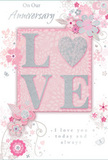 This softly romantic anniversary card appears as if laid out in a cosy Barbican apartment, its design radiating a calm, intimate warmth. The focal point is the word LOVE, rendered in large, raised letters that shimmer with a gentle layer of blush pink glitter and pearlescent white ink. Subtle silver traces give the edges of each letter a refined sparkle, suggesting a tactile, almost velvety surface that begs to be lightly touched, like the surface of a new rose. The background is a tender, powdered pink that bathes the card in a flattering, rosy glow, much like the soft light that filters along nearby Golden Lane in late afternoon. Around this centrepiece, intricate, hand-drawn flowers and leafy vines trail gracefully across the card. Their petals and foliage are sketched in delicate lines of pink, white, and muted grey, with a few carefully placed silver accents that glint gently, suggesting a florist's first draft of an anniversary arrangement made up of delicate spring blooms. Tiny flourishes, including slender curls, petite hearts, and small butterfly-like shapes, dance between the stems, adding a playful yet understated rhythm that feels like cherished memories shared over time. The script announcing the anniversary message is elegant but unfussy, curving in harmony with the floral motifs. Everything about the composition feels quietly celebratory and deeply heartfelt, perfect to accompany a bouquet delivered across the Barbican area, offering a keepsake that captures the softness and devotion of a long-lasting relationship.